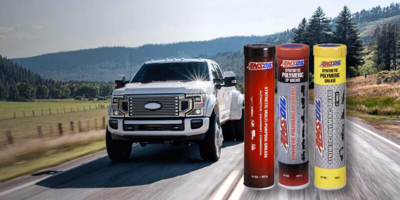 Three canisters of AMSOIL synthetic grease against the background of a diesel truck driving on a country road.